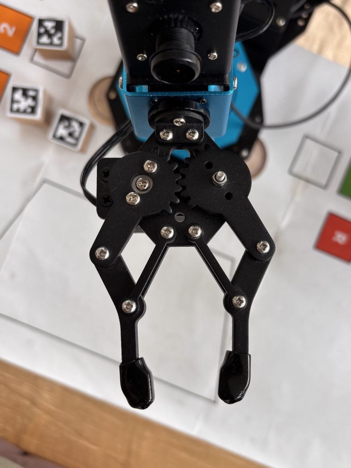 A black mechanical gripper is mounted below a small camera on a blue frame.