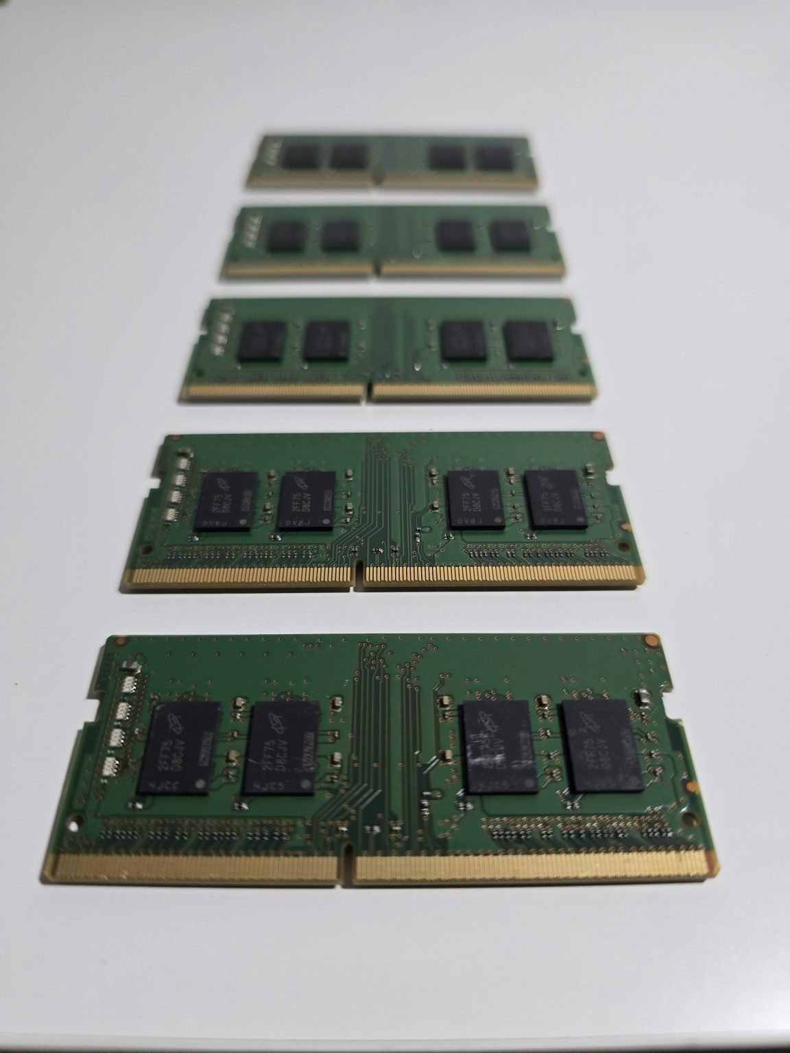 Five green laptop memory modules are arranged in a row on a pale surface.