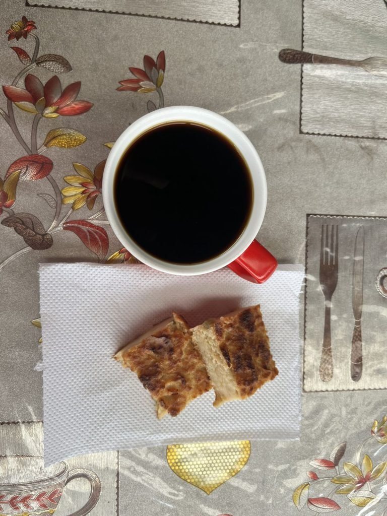 Overhead view of a red-handled mug of black coffee and two slices of toasted bread on a napkin, on a floral tablecloth.