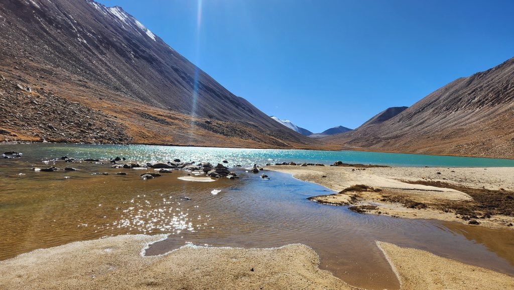 A turquoise lake below rocky, snow-capped mountains under a hazy sky