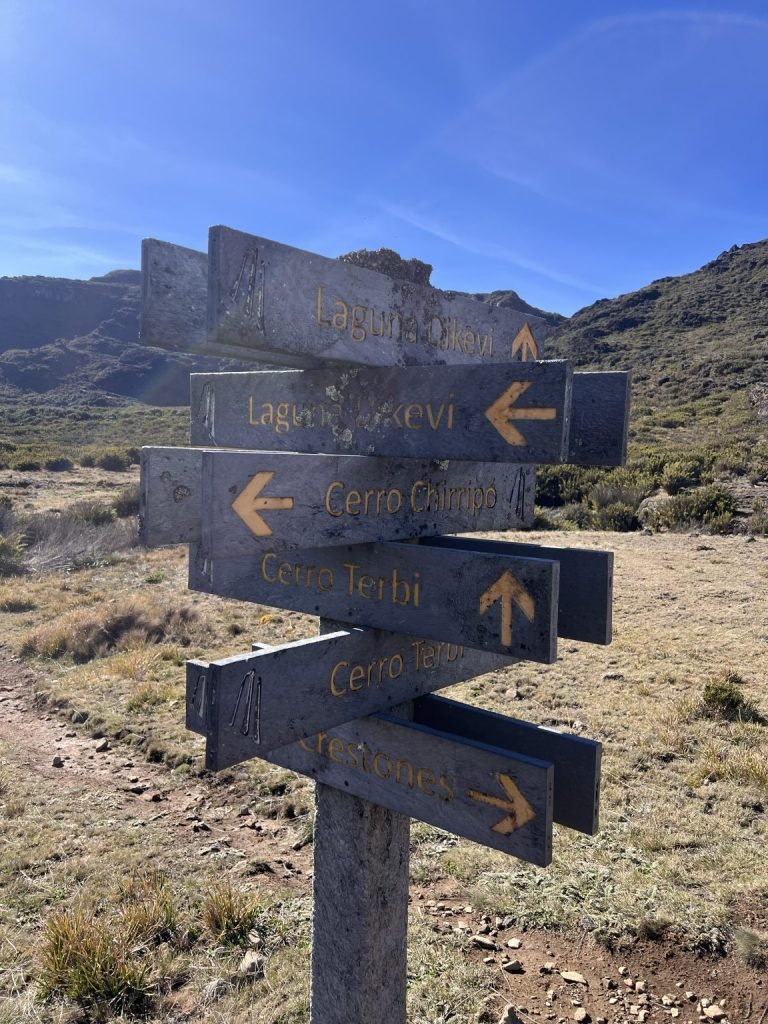 A wooden trail signpost pointing toward mountain hiking routes.