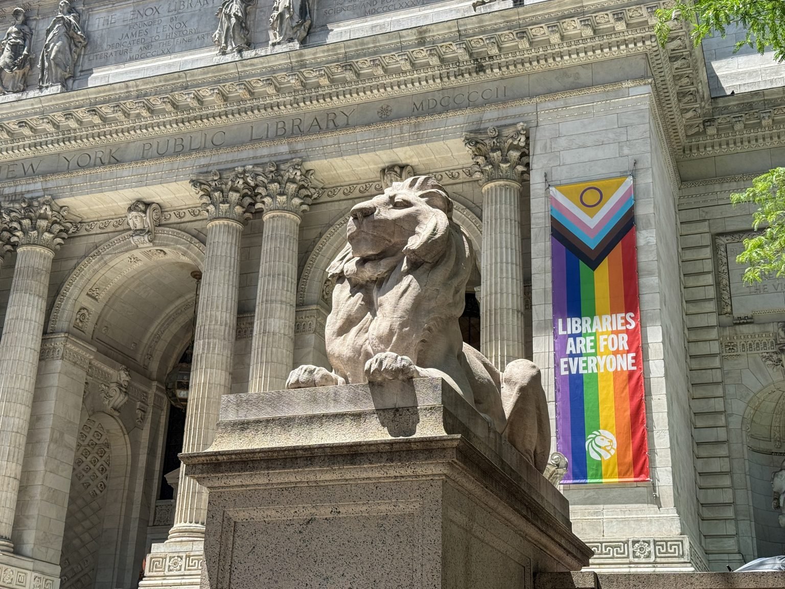 One of the stone lions outside the New York Public Library, with a perpendicular pride banner that says 'Libraries are for Everyone'