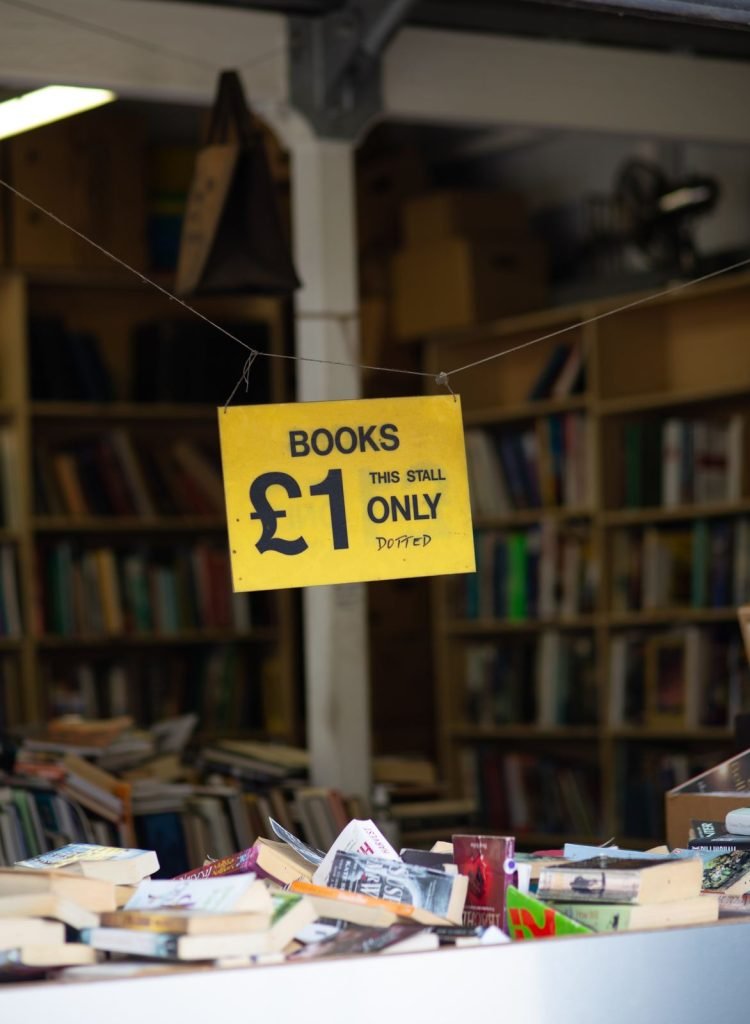 A yellow sign reading Books £1 hangs over a stall of used books in front of tall shelves.
