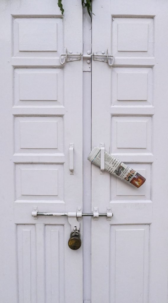 A rolled newspaper tucked into the handle of a white panelled shop door.