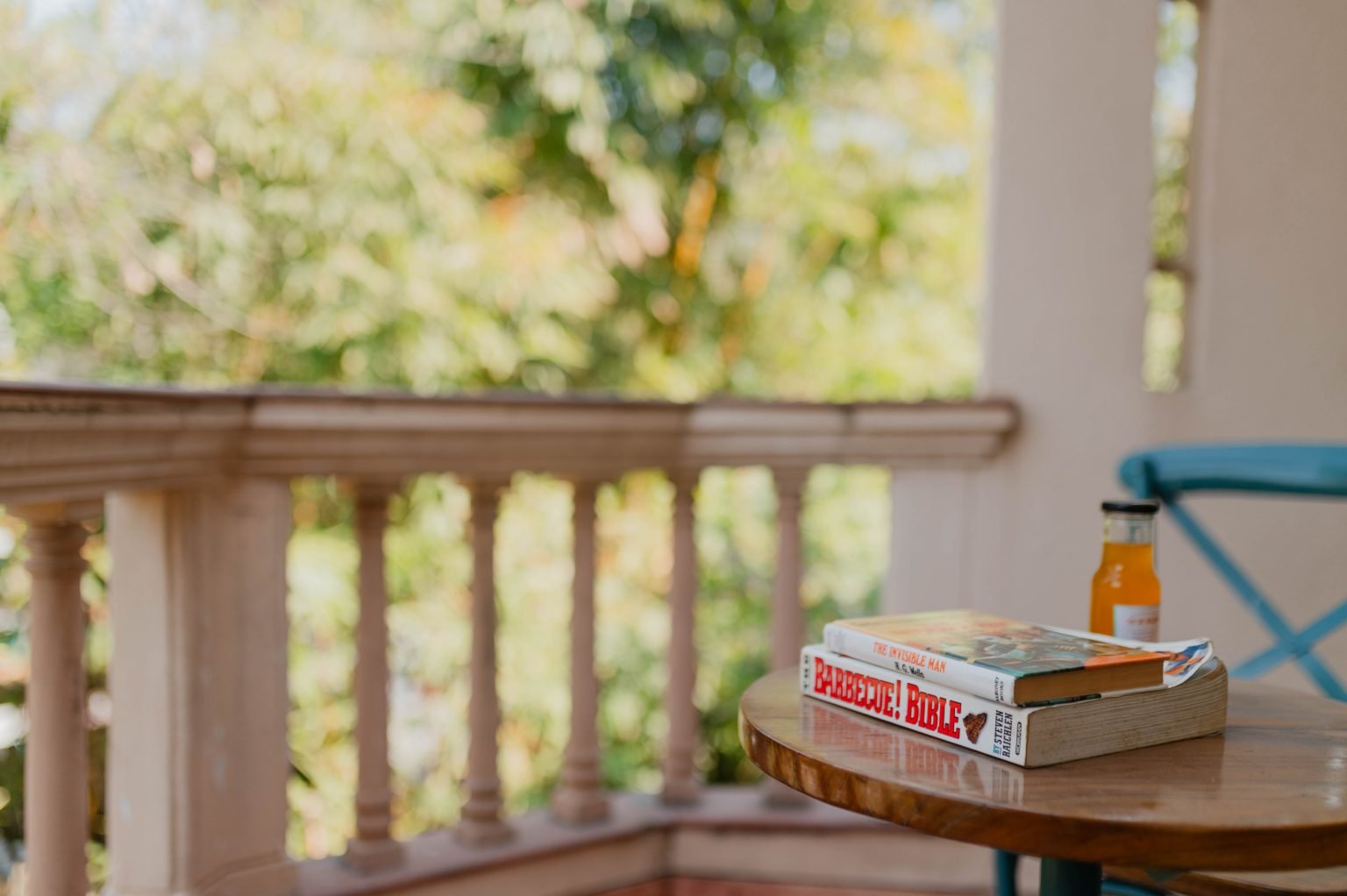 Books and a bottle sit on a small table beside a balcony railing and a blue chair.