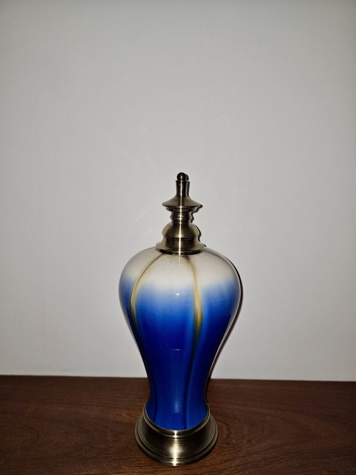 A blue-and-white decorative bottle with a metal lid stands on a wooden surface against a plain wall.