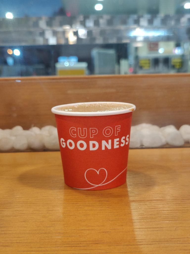 A red paper cup filled with a frothy hot coffee sits on a wooden table