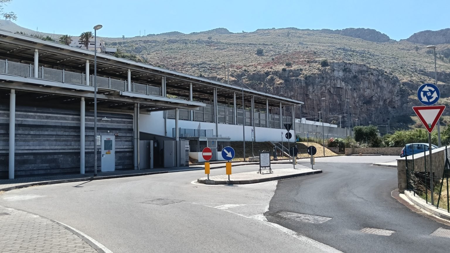 Small road with traffic signals and parking next to a train station over a tropical valley.