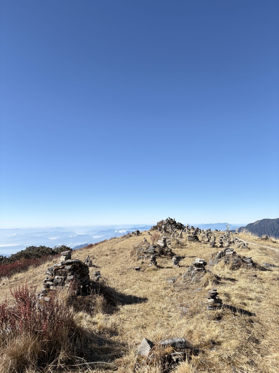 Small stone cairns stand on a grassy ridge beneath a wide blue sky.