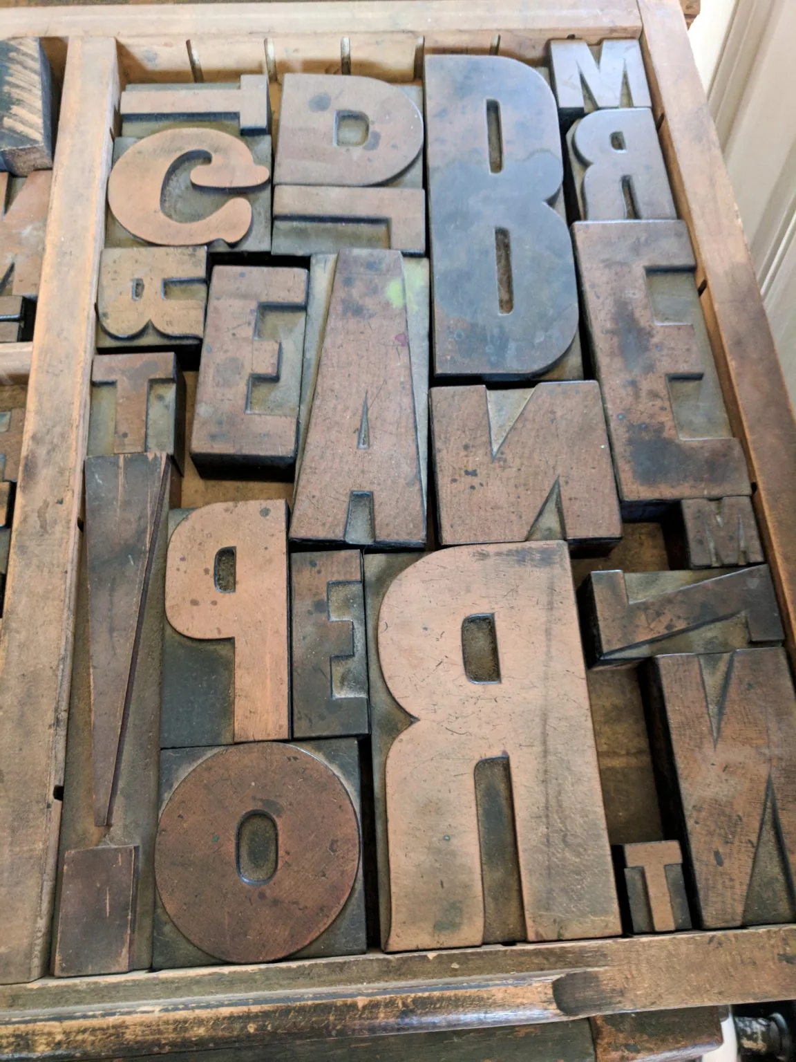 Worn wooden printing letters fill a shallow tray.