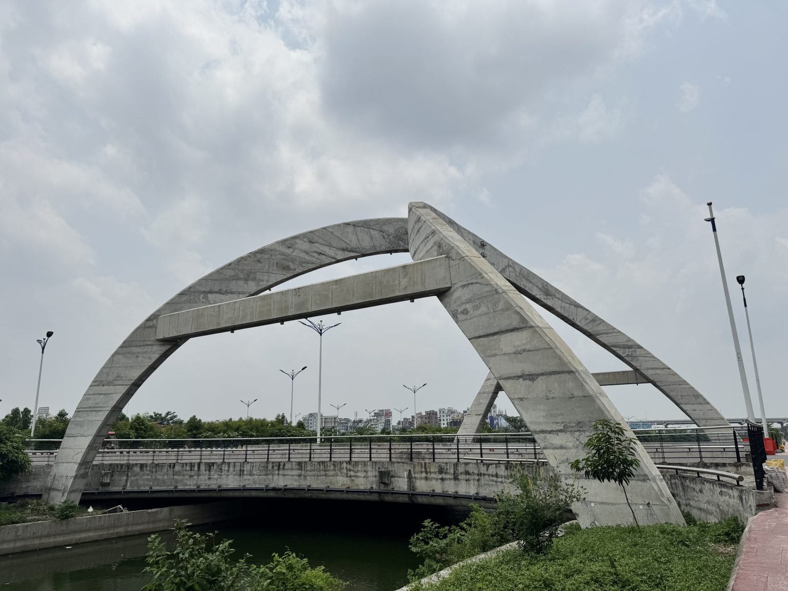 A concrete arch bridge beneath a cloudy sky, with a staircase and green vegetation below.