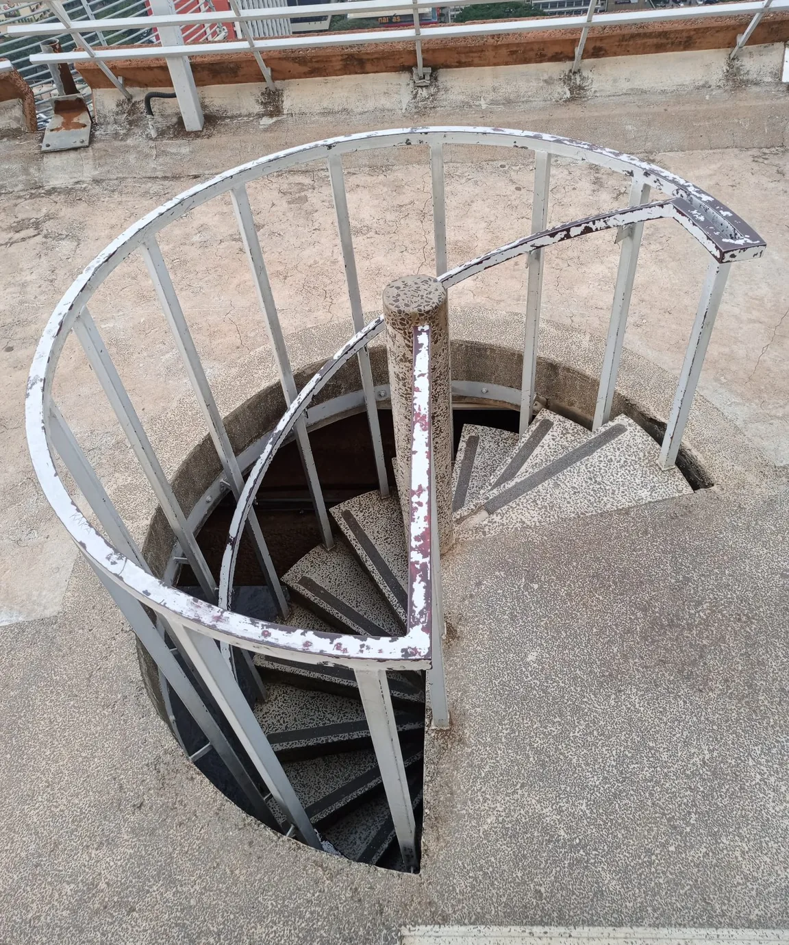 A spiral staircase with speckled treads and a weathered white handrail, viewed from above.