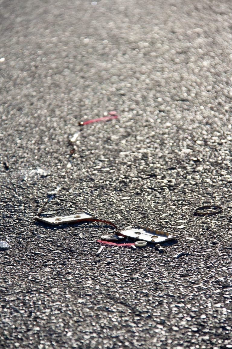 A broken cassette and loose tape lie on sunlit asphalt.